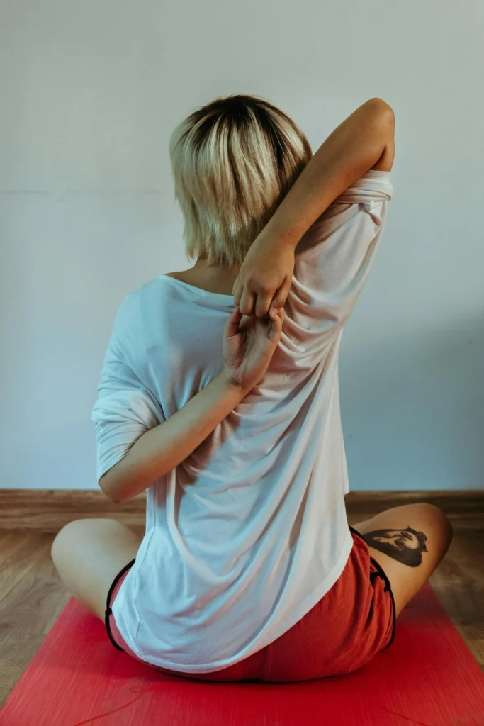 Femme qui s'étire et se fait craquer le dos et épaules en position assise depuis chez elle sur un tapis