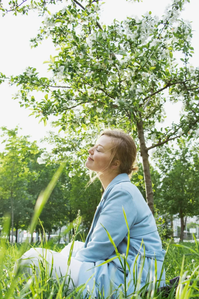 Femme sereine assise dans la nature qui respire les yeux fermés avec confiance.